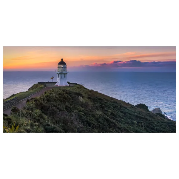 Cape Reinga lighthouse at sunset with a path leading to it and rocks at the bottom.