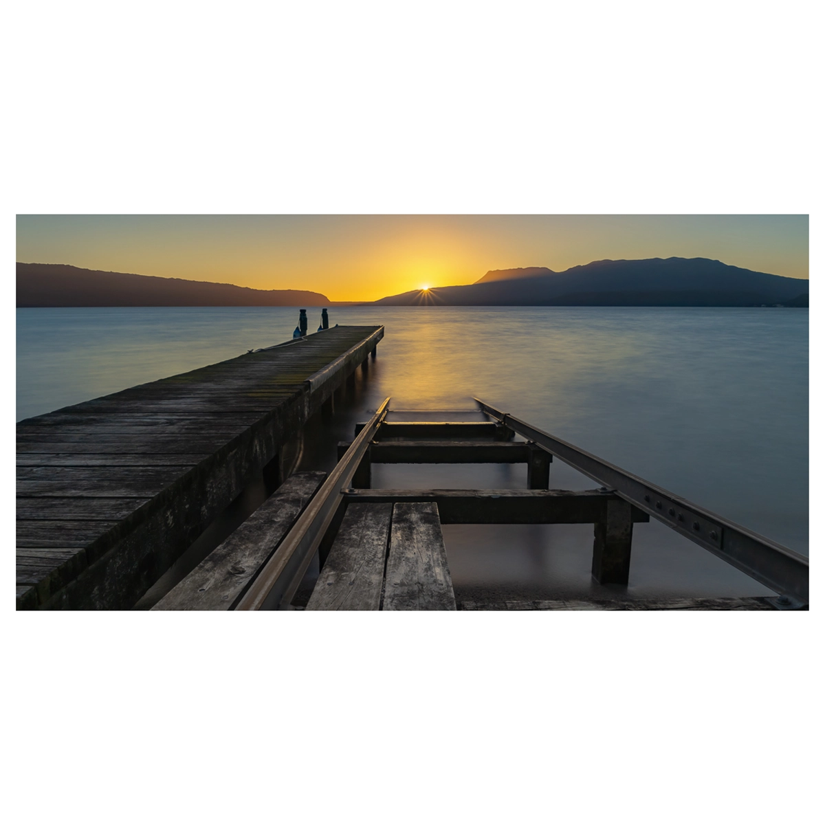 Sunrise at Lake Tarawera with a starburst effect over the lake, viewed from a jetty.