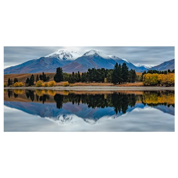 Long exposure photo of Lake Camp, Ashburton Lakes, early morning with reflections of autumn trees and snow-capped mountains.