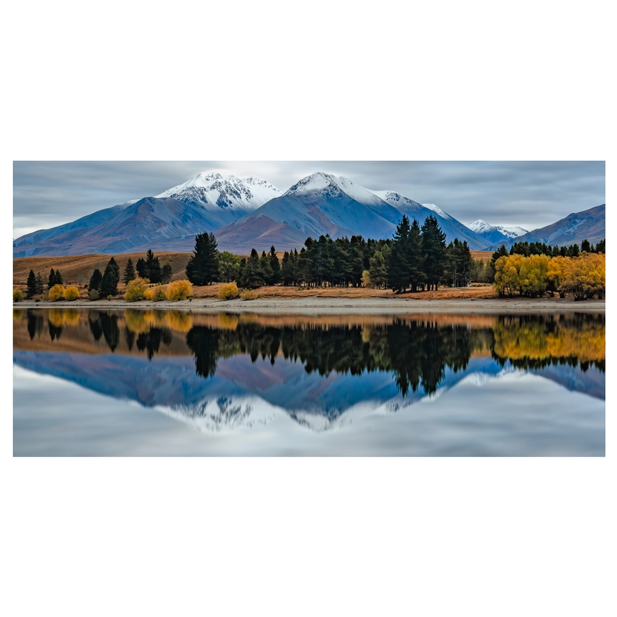 Long exposure photo of Lake Camp, Ashburton Lakes, early morning with reflections of autumn trees and snow-capped mountains.