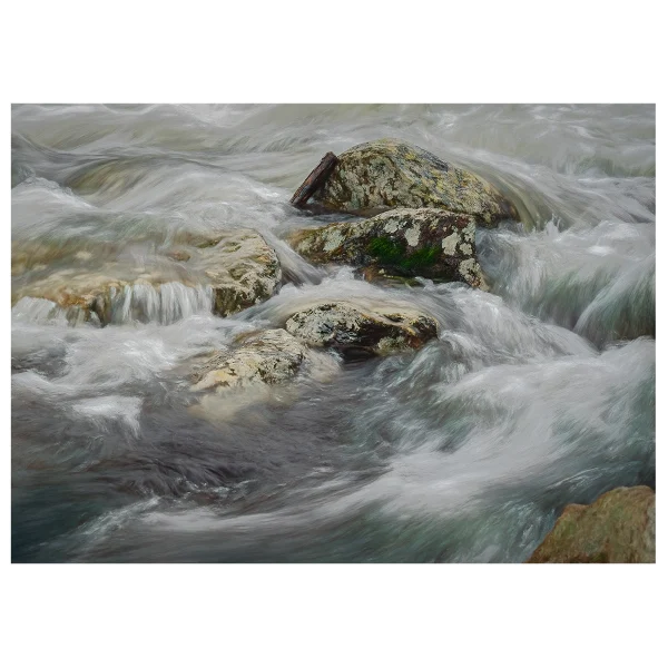 Close-up long exposure of water rushing around rocks in a river, with detailed flow patterns