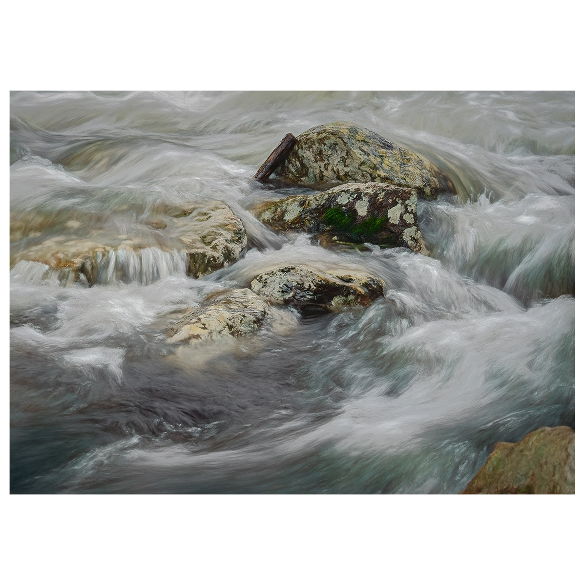 Close-up long exposure of water rushing around rocks in a river, with detailed flow patterns