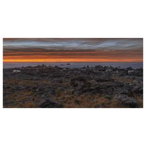 Sunrise on the Kaikoura coast with an orange horizon, rocky foreground, and long exposure effect.