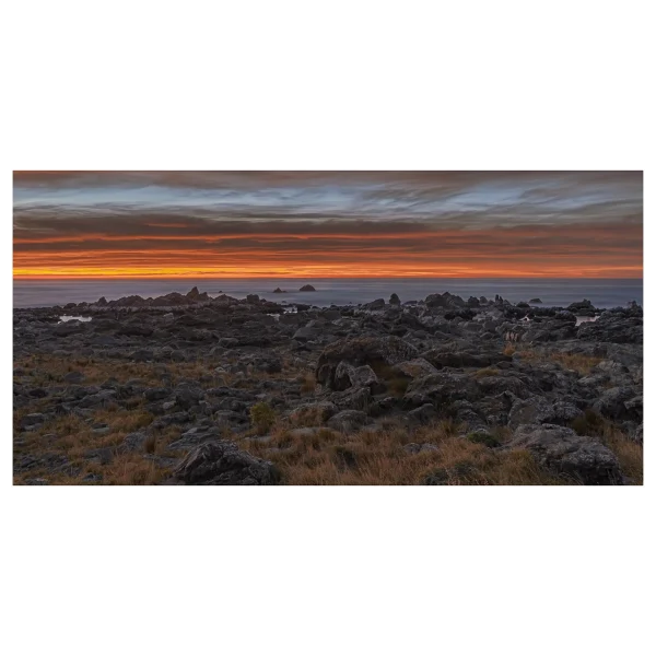 Sunrise on the Kaikoura coast with an orange horizon, rocky foreground, and long exposure effect.