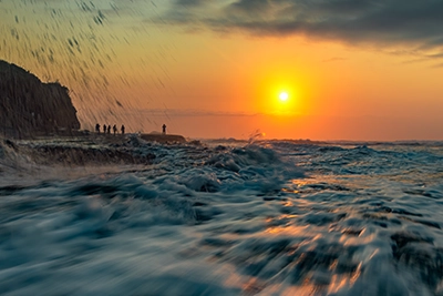 Close-up of a rogue wave at Muriwai Beach moments before it crashes, with a golden sunset glowing in the background.