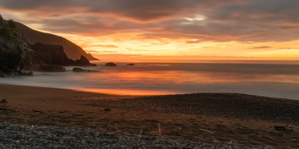 Rarangi Beach Sunrise – Long Exposure with Pebbly Beach, Rocks, and Orange Sky