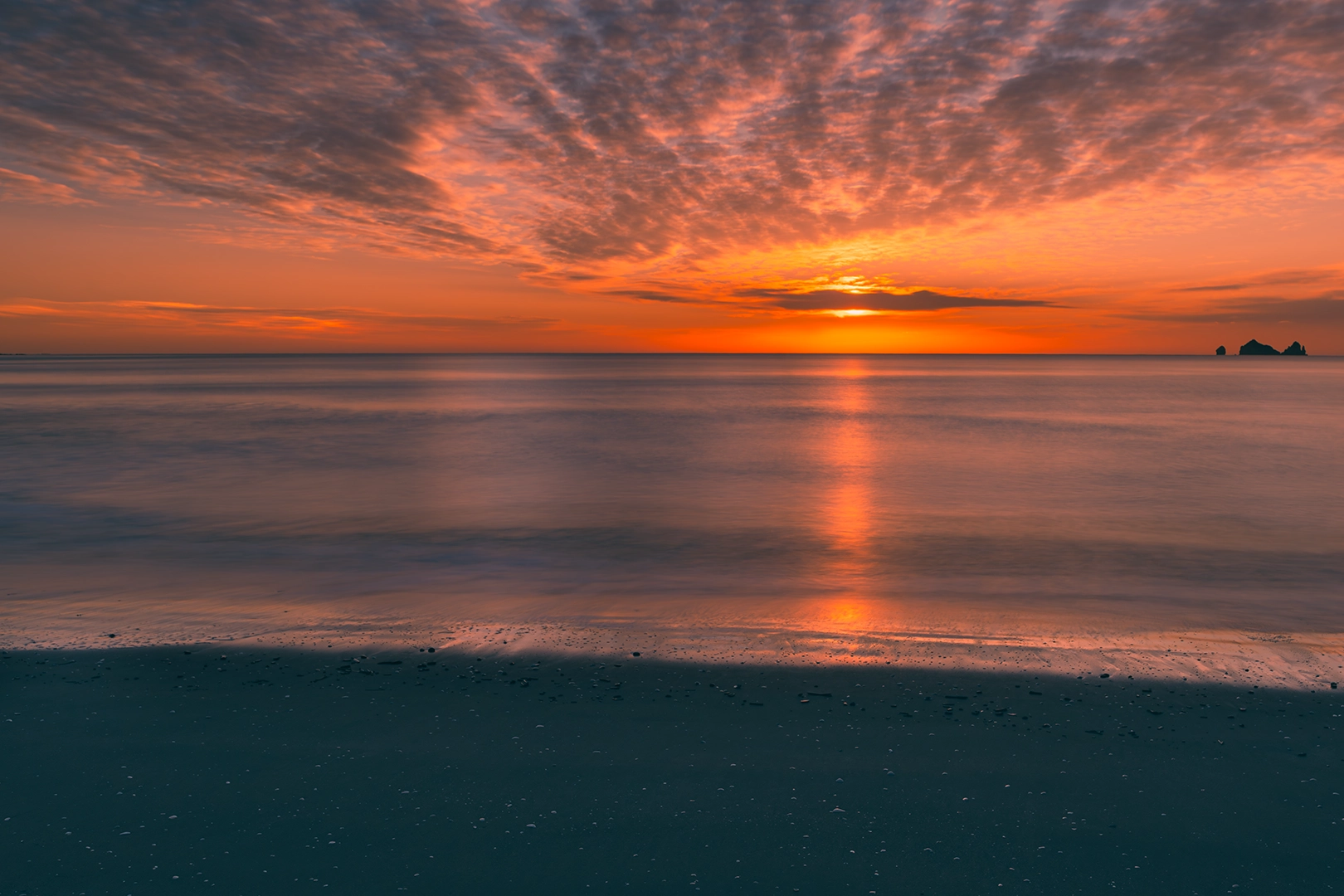 Tolaga Bay Long Exposure Sunrise – Dark Sand, Blue Sea, and Orange Sky