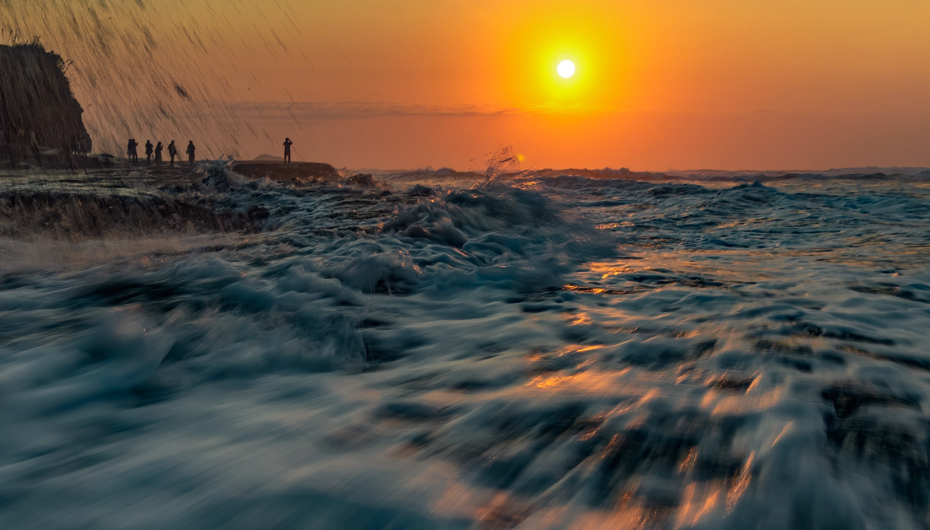 A wave rushing up Muriwai beach while photographing the sunset